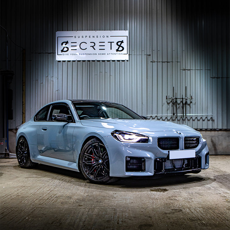 Suspension Secrets adjustable camber and caster plates kit for BMW G87 M2 showing metal plates with mounting hardware and adjustment bolts.