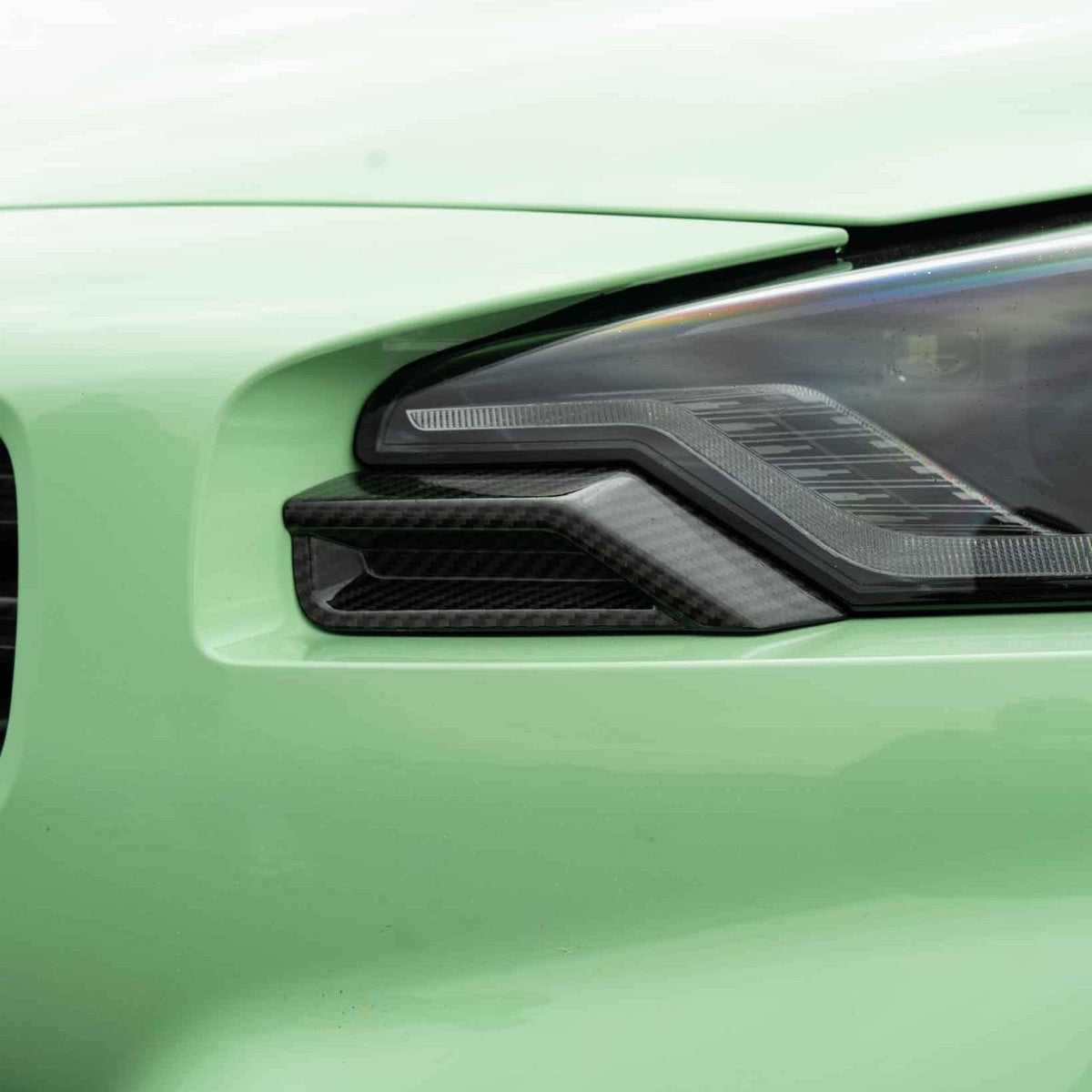 BMW G87 M2 carbon fiber front headlight add-on accessory by CT Carbon, featuring sleek carbon fiber details and precise fitment.