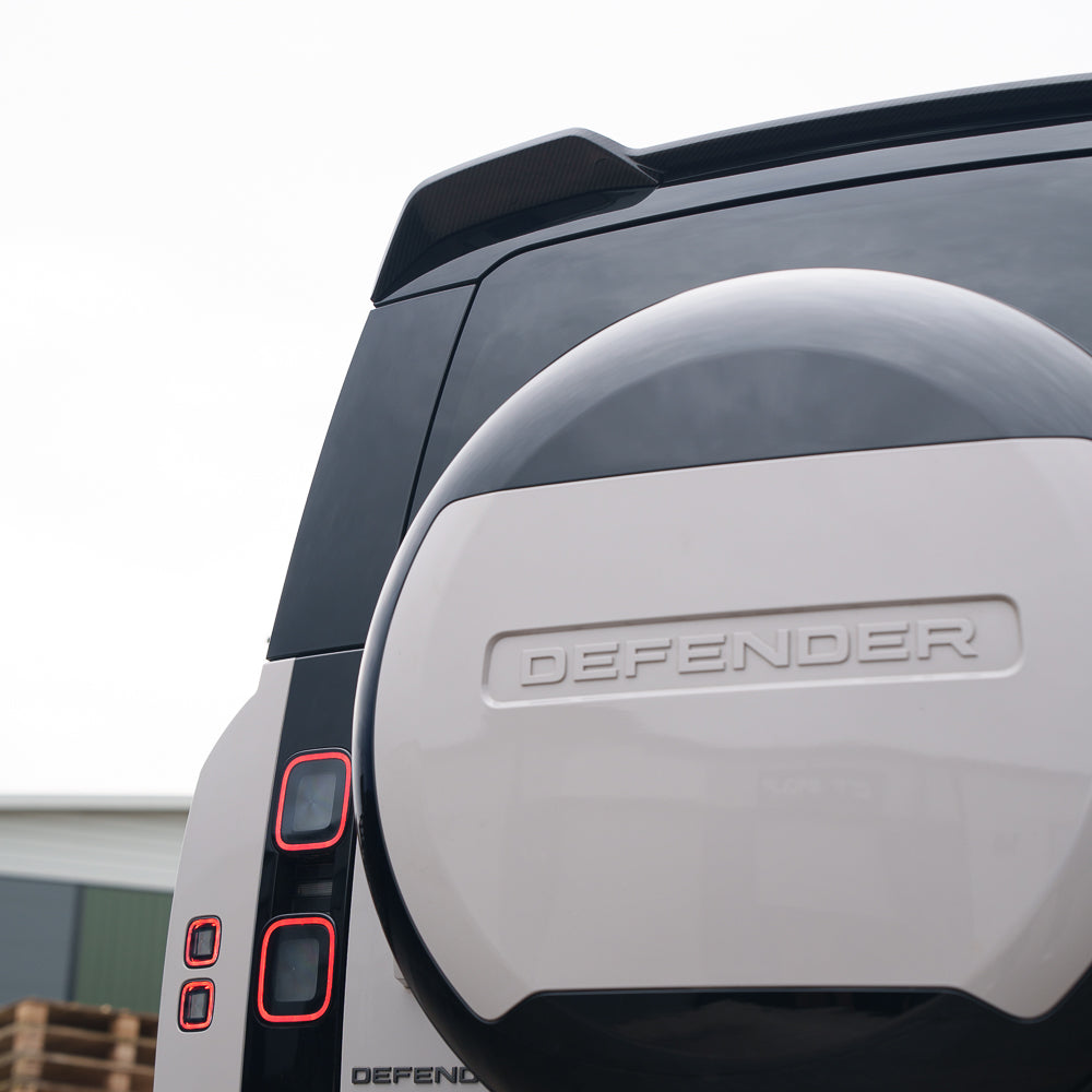 Land Rover Defender L663 carbon fiber spoiler by CT Carbon, sleek aerodynamic car accessory on a black vehicle.