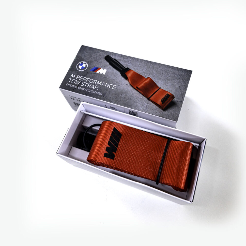 Genuine BMW M Performance red tow strap for M2 F87 G87 M3 G80 G20 G42, securely attached to vehicle's front or rear.