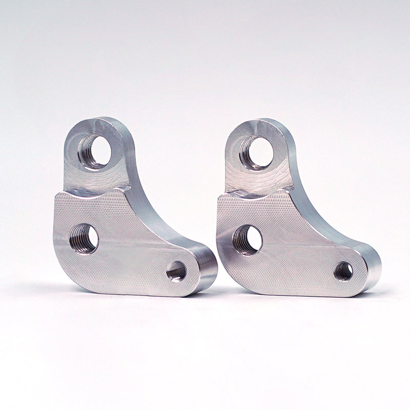 Pair of Suspension Secrets seat raisers for Porsche 718 GT4 RS suspension linkages, shown installed on vehicle seat area.