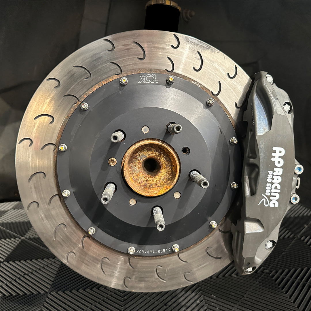 BMW M3 E9X/E92 BTCC brake upgrade kit with AP Racing caliper carrier and rotor bell, installed on car for enhanced braking performance.